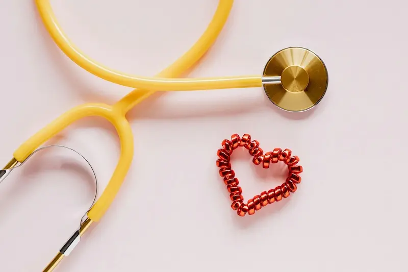 Yellow stethoscope and red beaded heart symbol on a light pink background, representing heart failure cardiac care